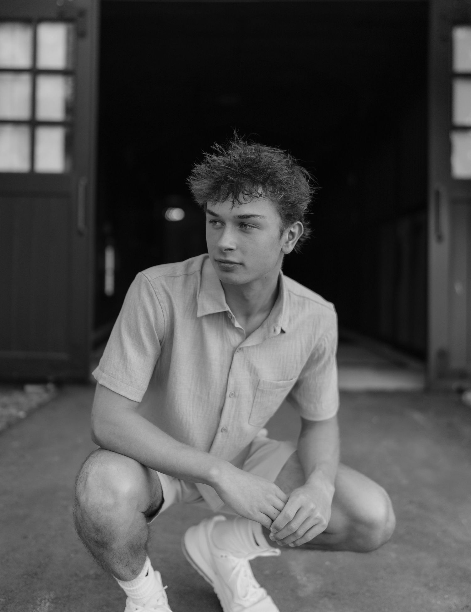Young man crouching in front of barn doors in a vintage black and white portrait photo.