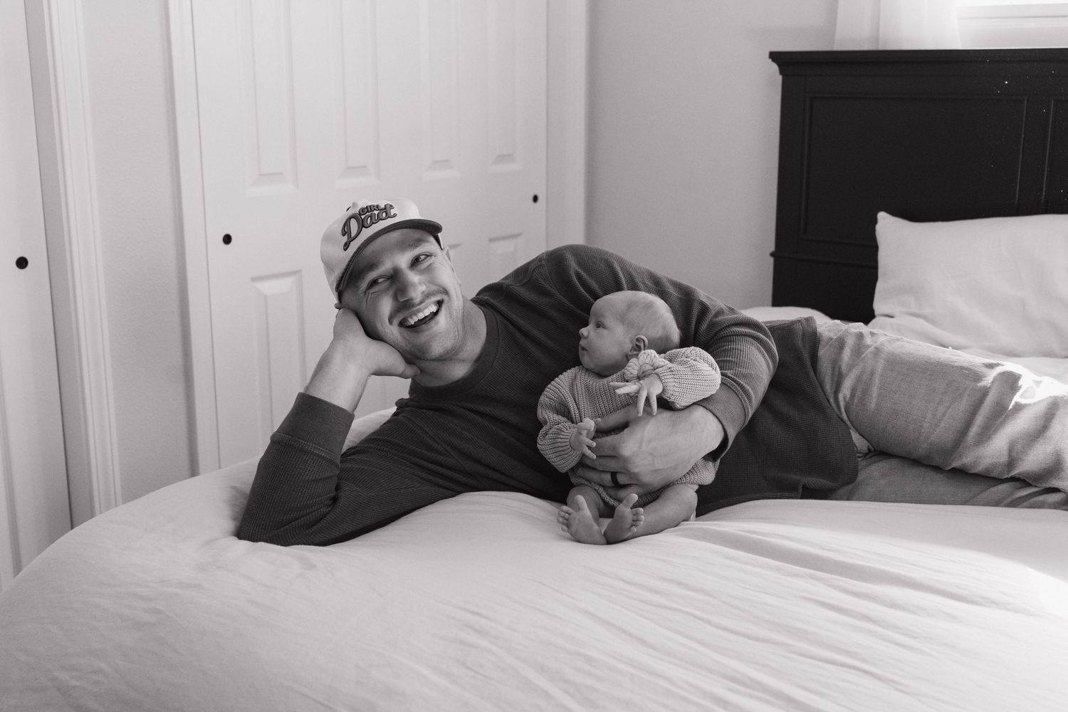 A man lying on a bed, smiling and holding a baby.