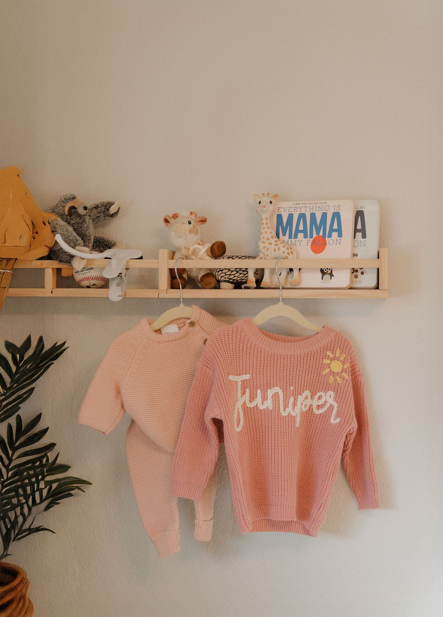 A cozy nursery with pink sweaters and a decorative sign that says 'Mama' on a wooden shelf.