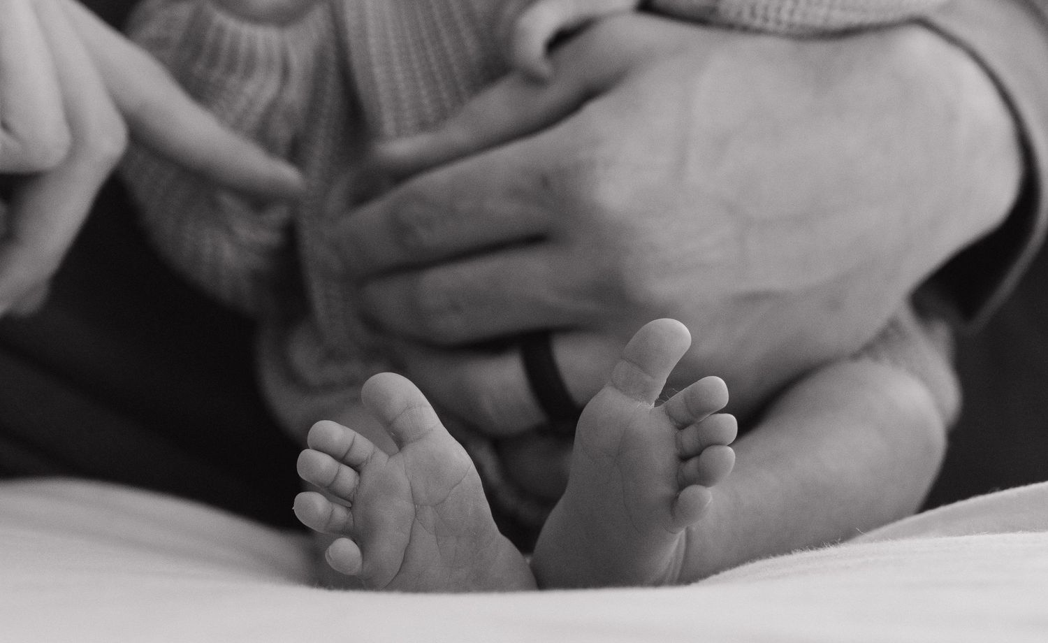 A close-up black and white image of a newborn baby's feet resting on a soft surface.
