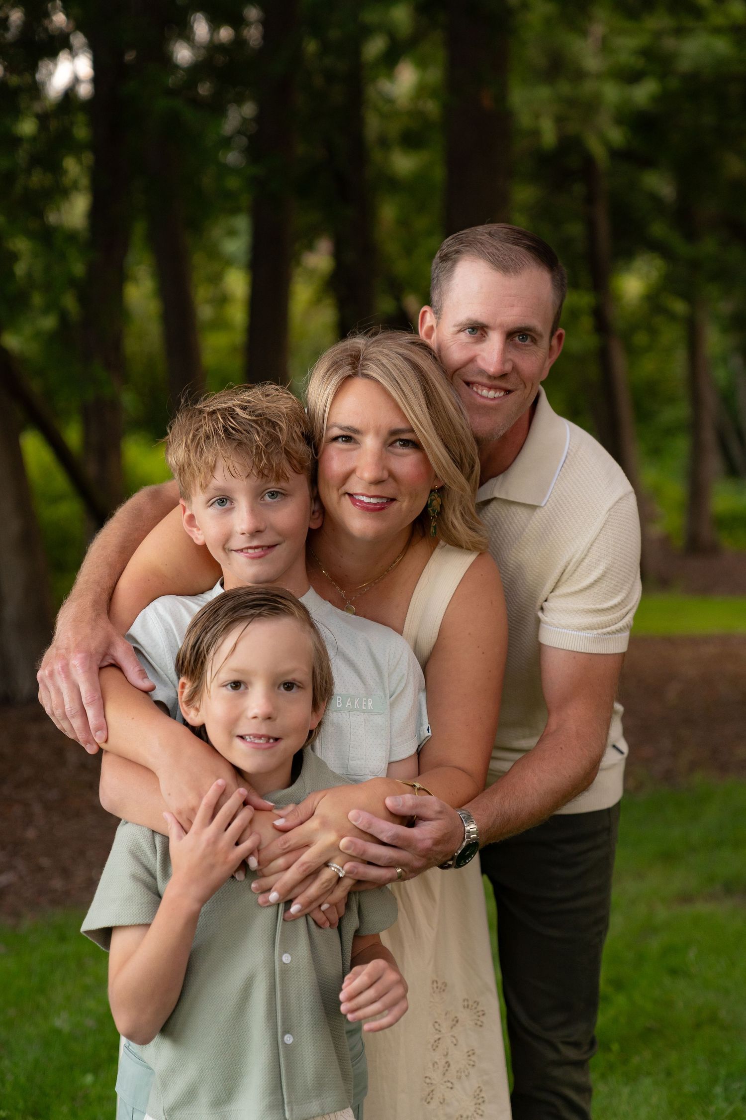 A happy family of four, including a mother, father, and two children, posing together in a park setting.