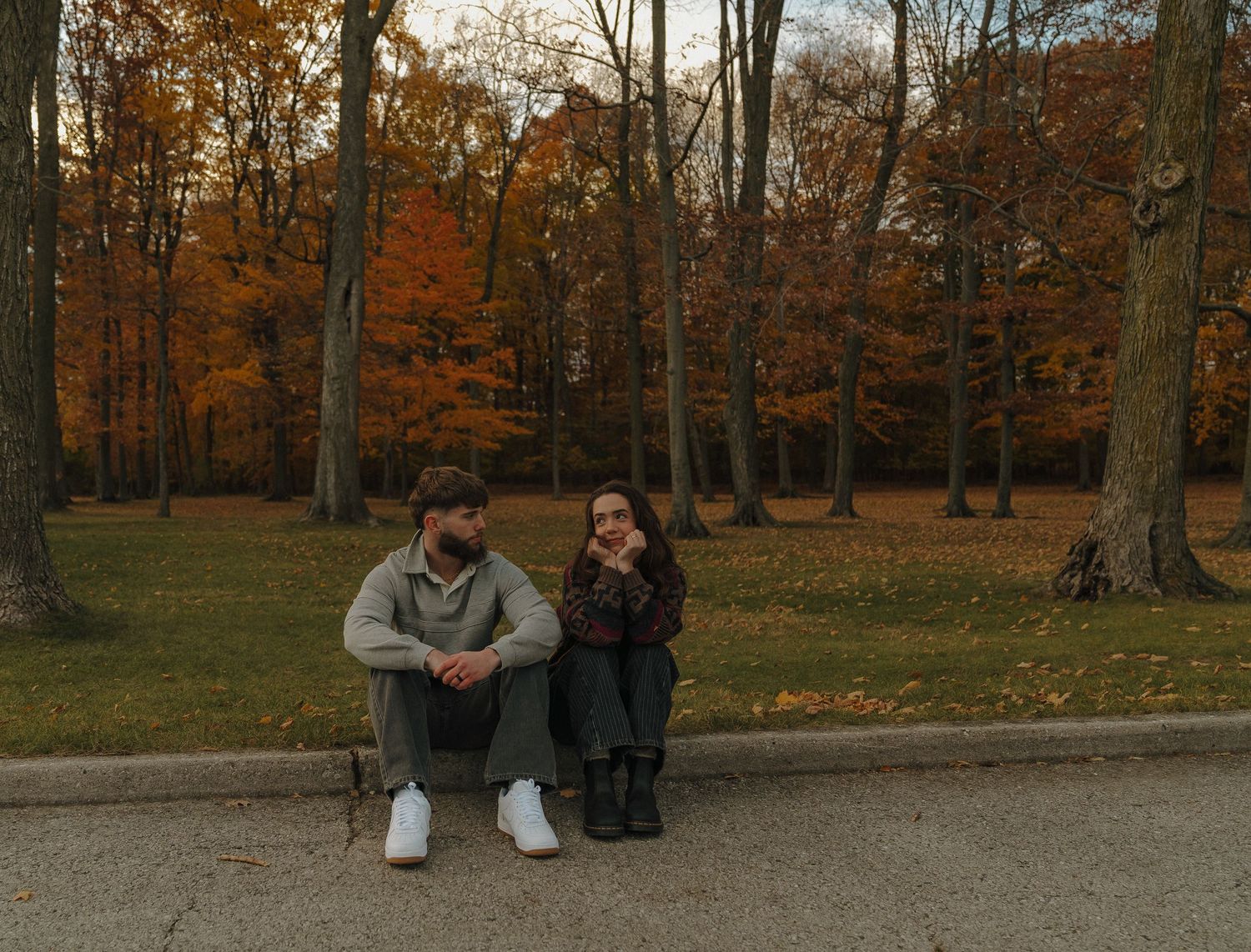 Two people sitting on a bench in a park surrounded by autumn foliage.