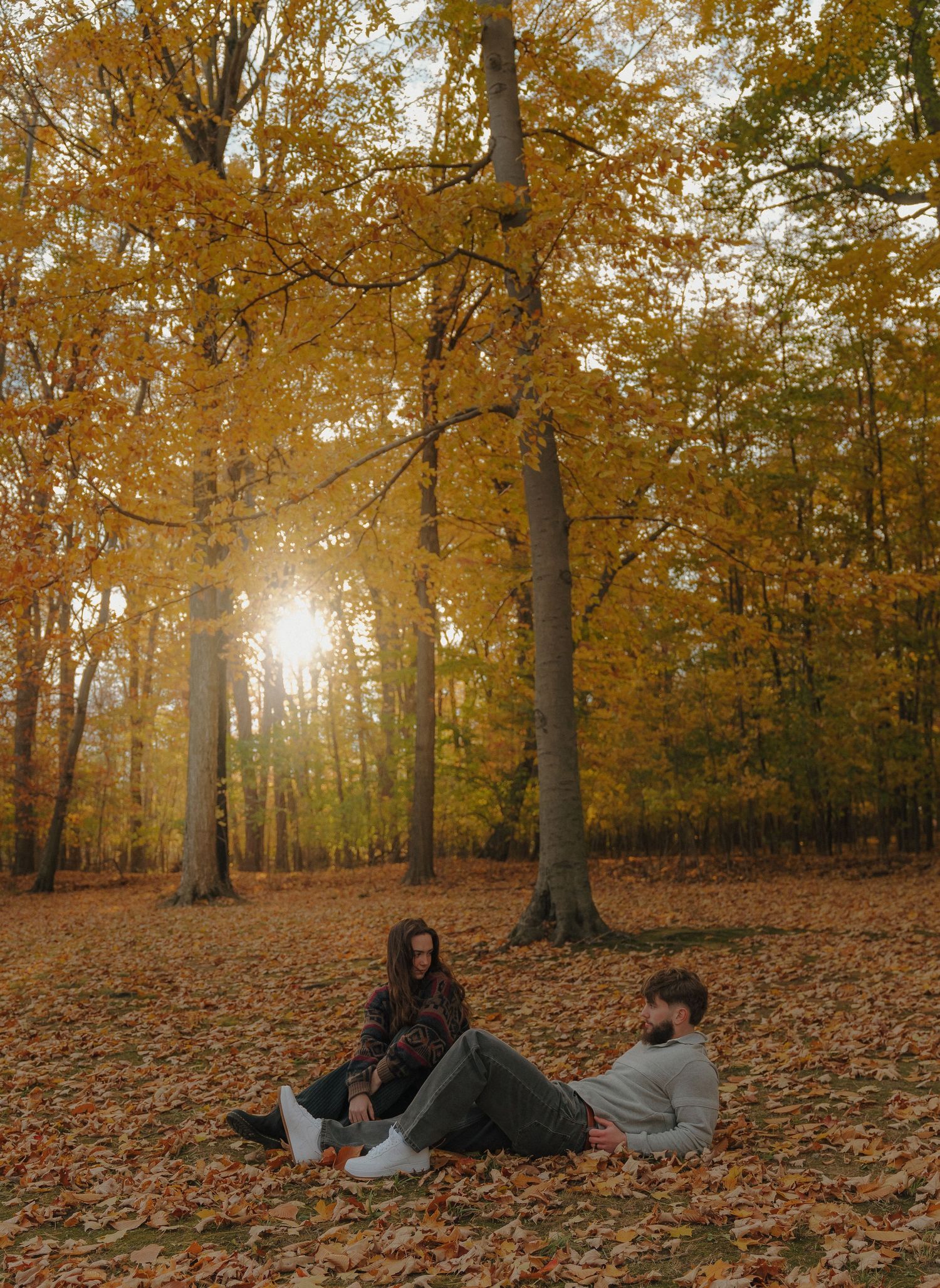The image shows a group of people sitting on the ground in a forest with vibrant autumn foliage surrounding them.