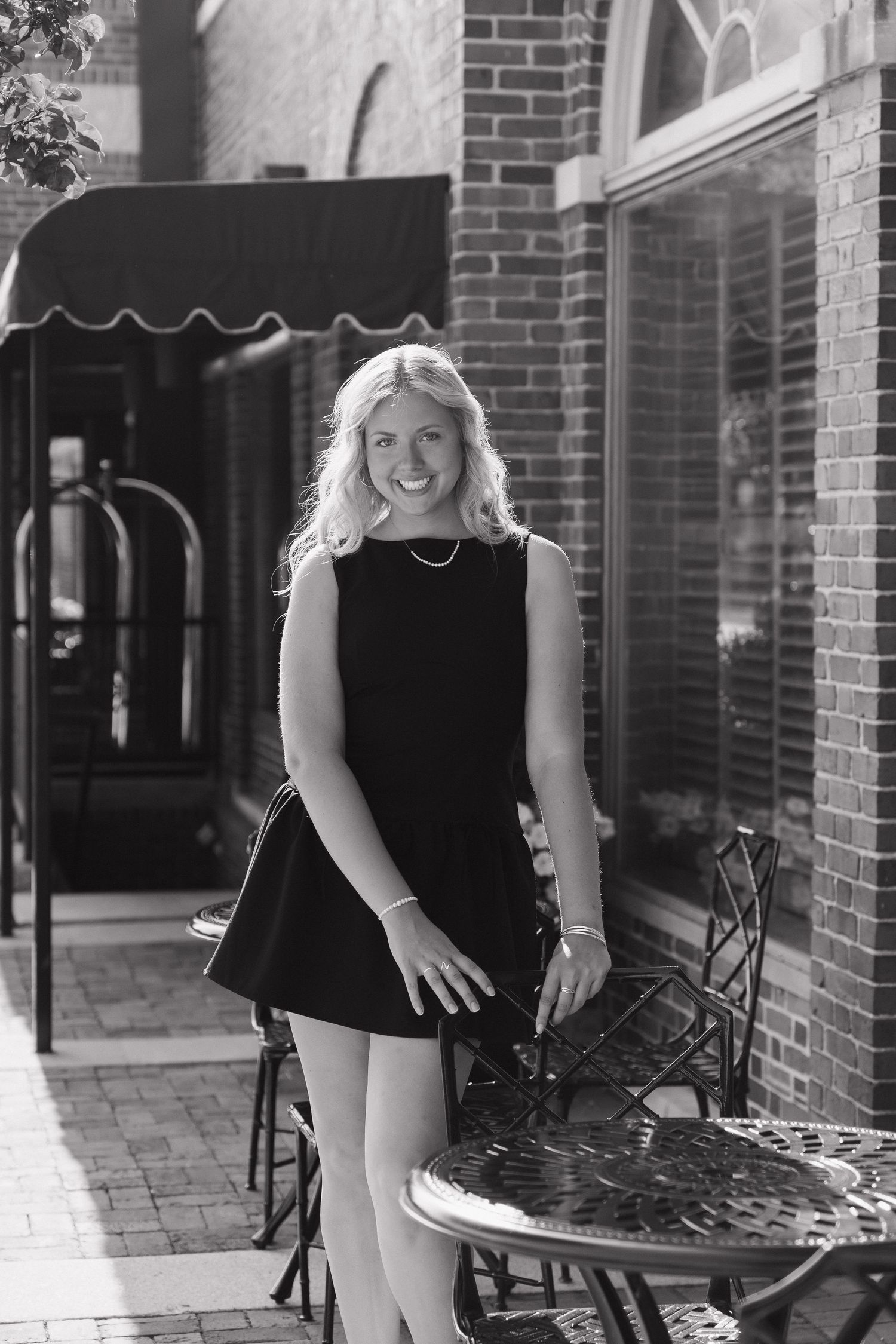 A young woman with blonde hair is smiling and standing in front of a brick building.