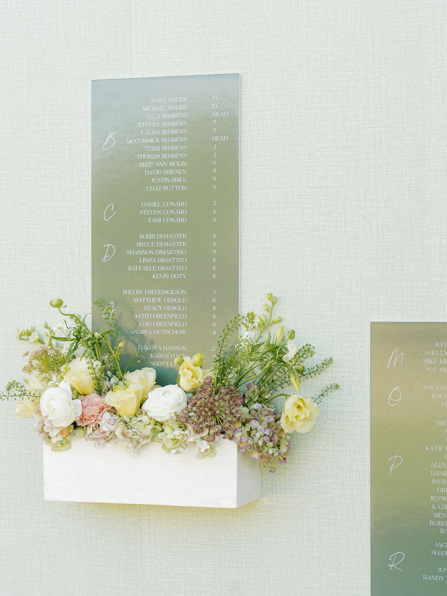 Elegant wedding seating chart on mirrored panel with white floral arrangement in white box planter.