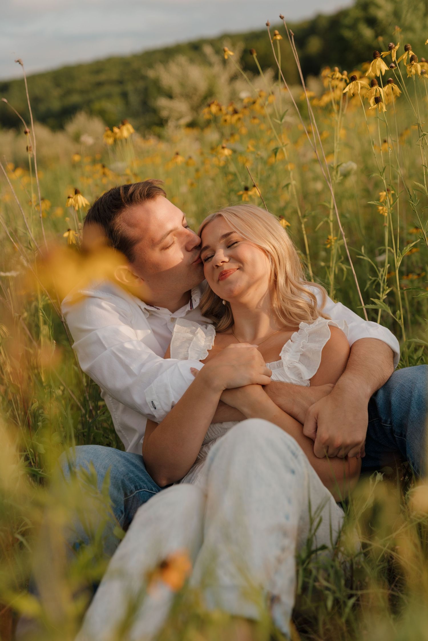 Romantic couple sitting in a sunny wildflower field, embracing among yellow blooms in golden hour light.