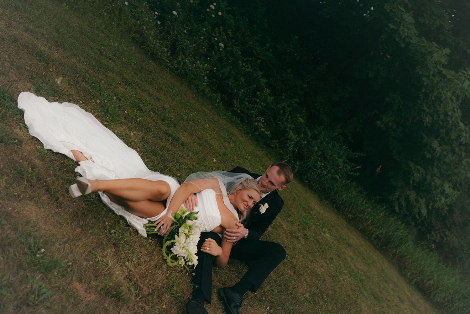 Aerial view of bride and groom sharing a romantic dip pose on green grass at outdoor wedding ceremony.