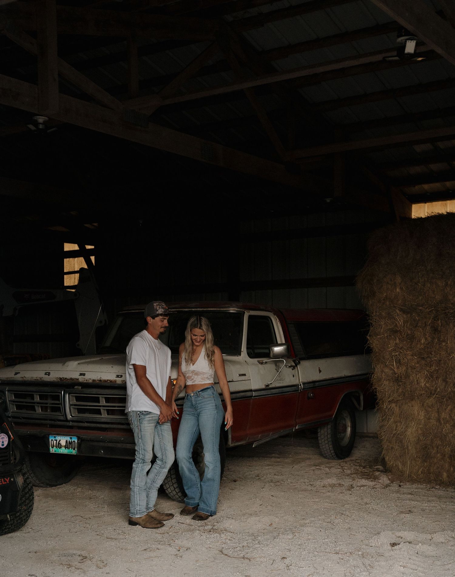 Two people stand next to a large truck in a dimly lit garage or barn.