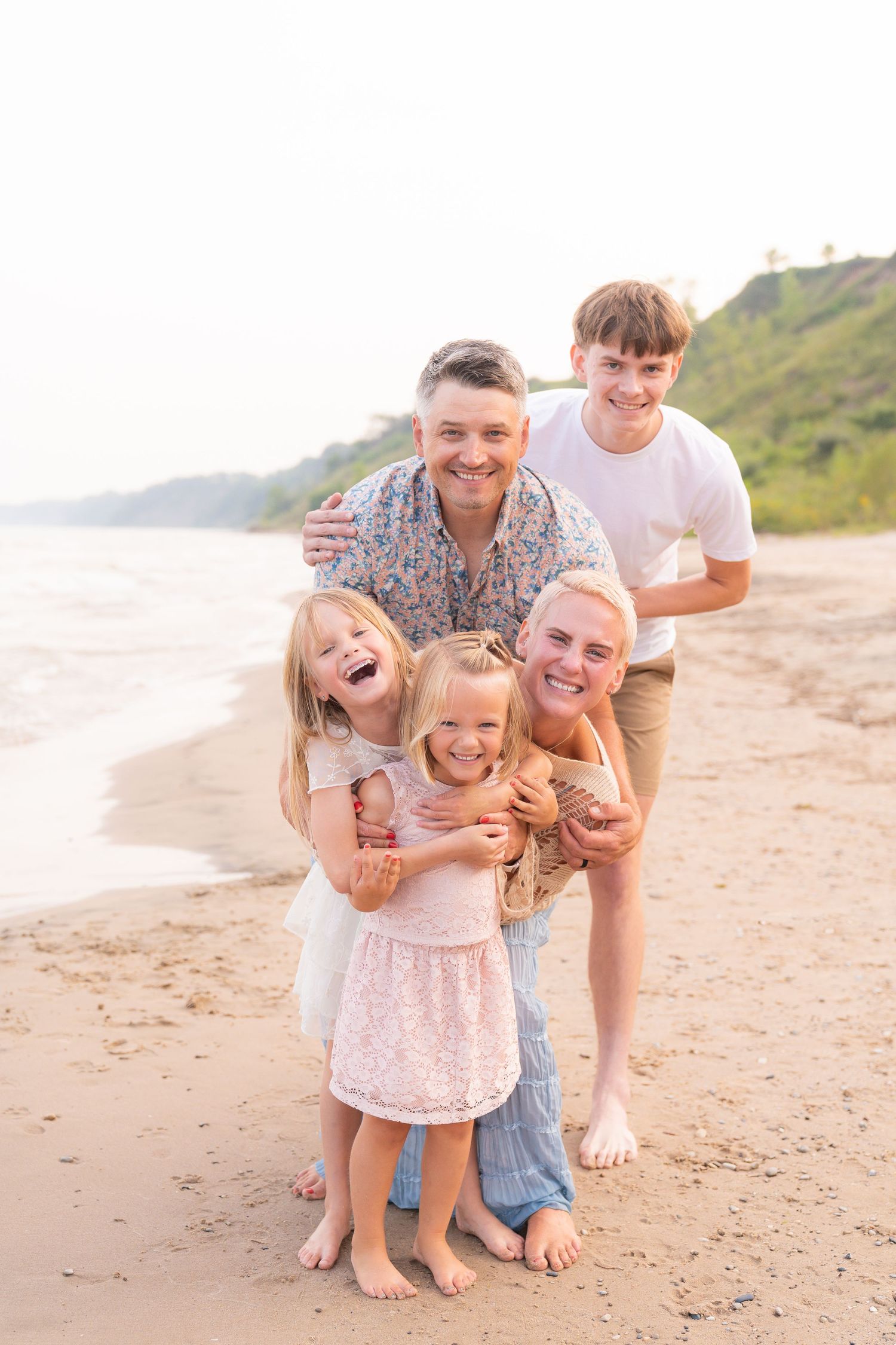 A family of five, including a mother, father, two daughters, and a son, standing together on a beach.