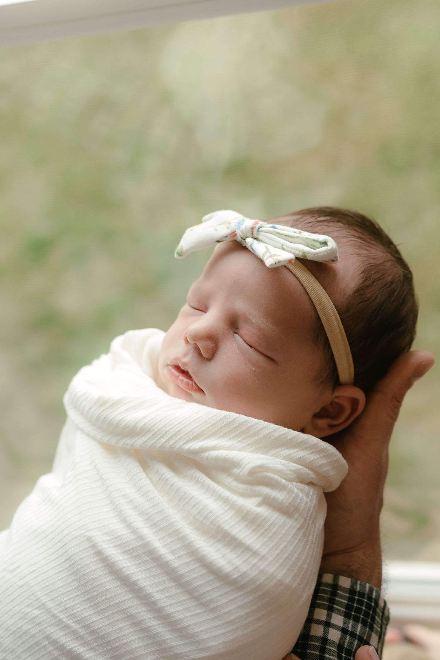 A newborn baby girl wrapped in a white blanket and wearing a headband with a bow, resting peacefully.