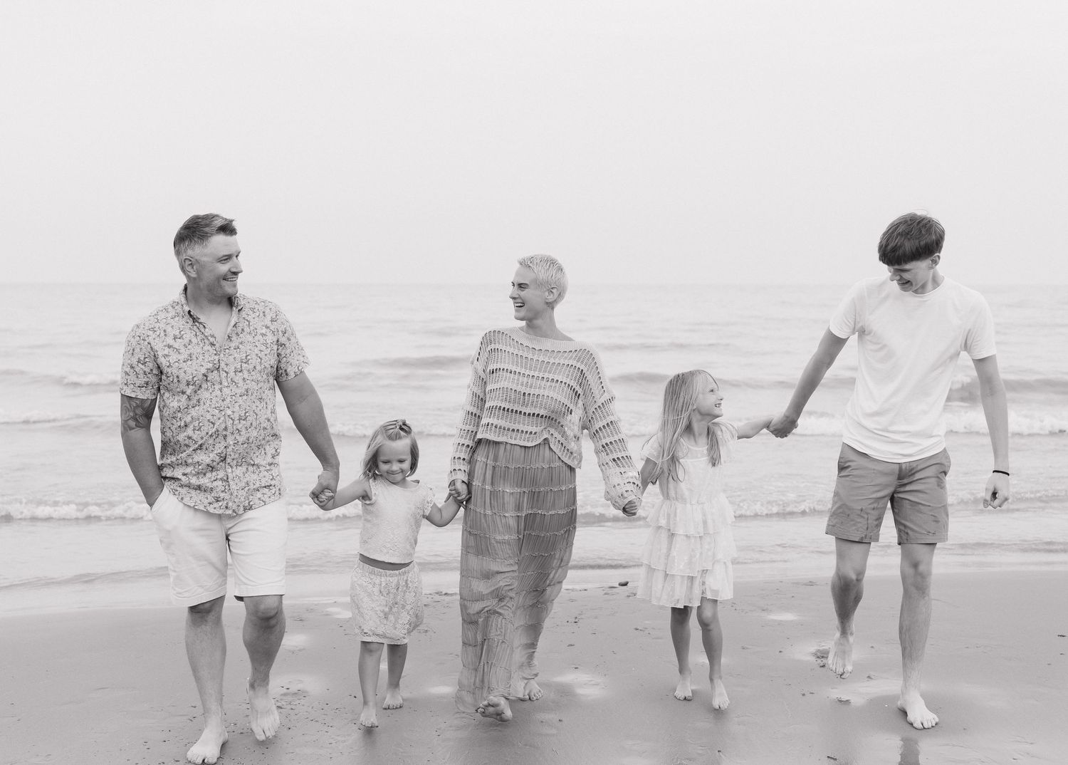 A family of four walking together on a beach, holding hands and enjoying the outdoors.
