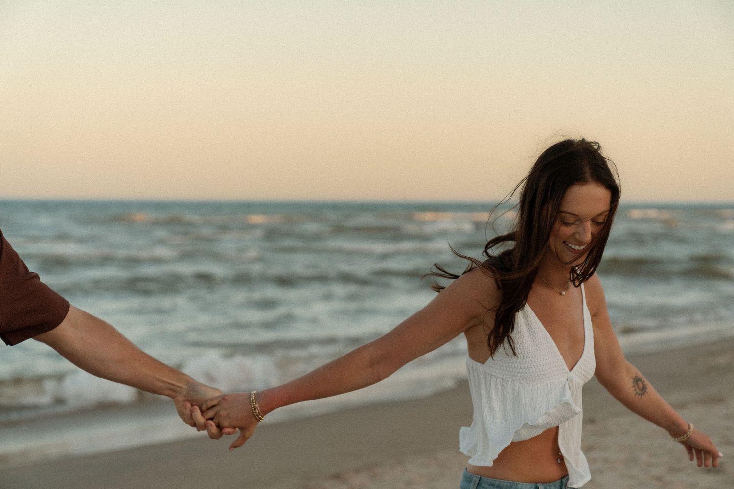 A couple holding hands while walking on a beach during sunset.