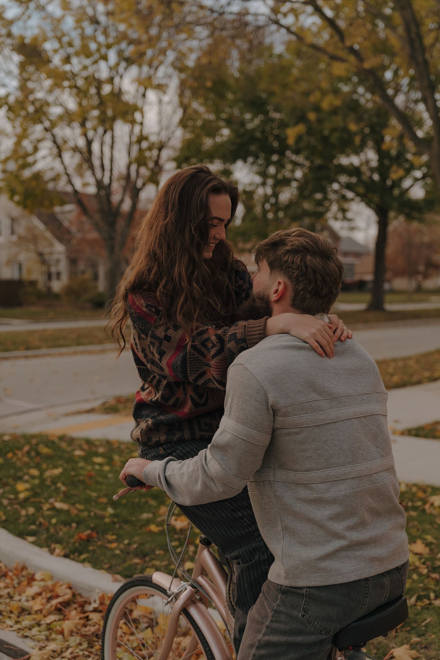 A young couple embracing while standing next to a bicycle on a path surrounded by autumn foliage.