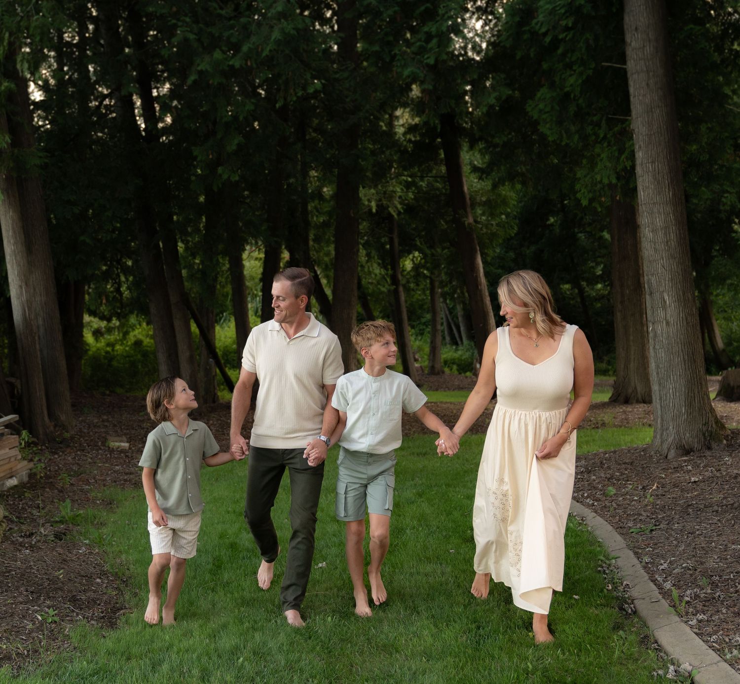 A family of four walks together on a path in a lush, wooded area.