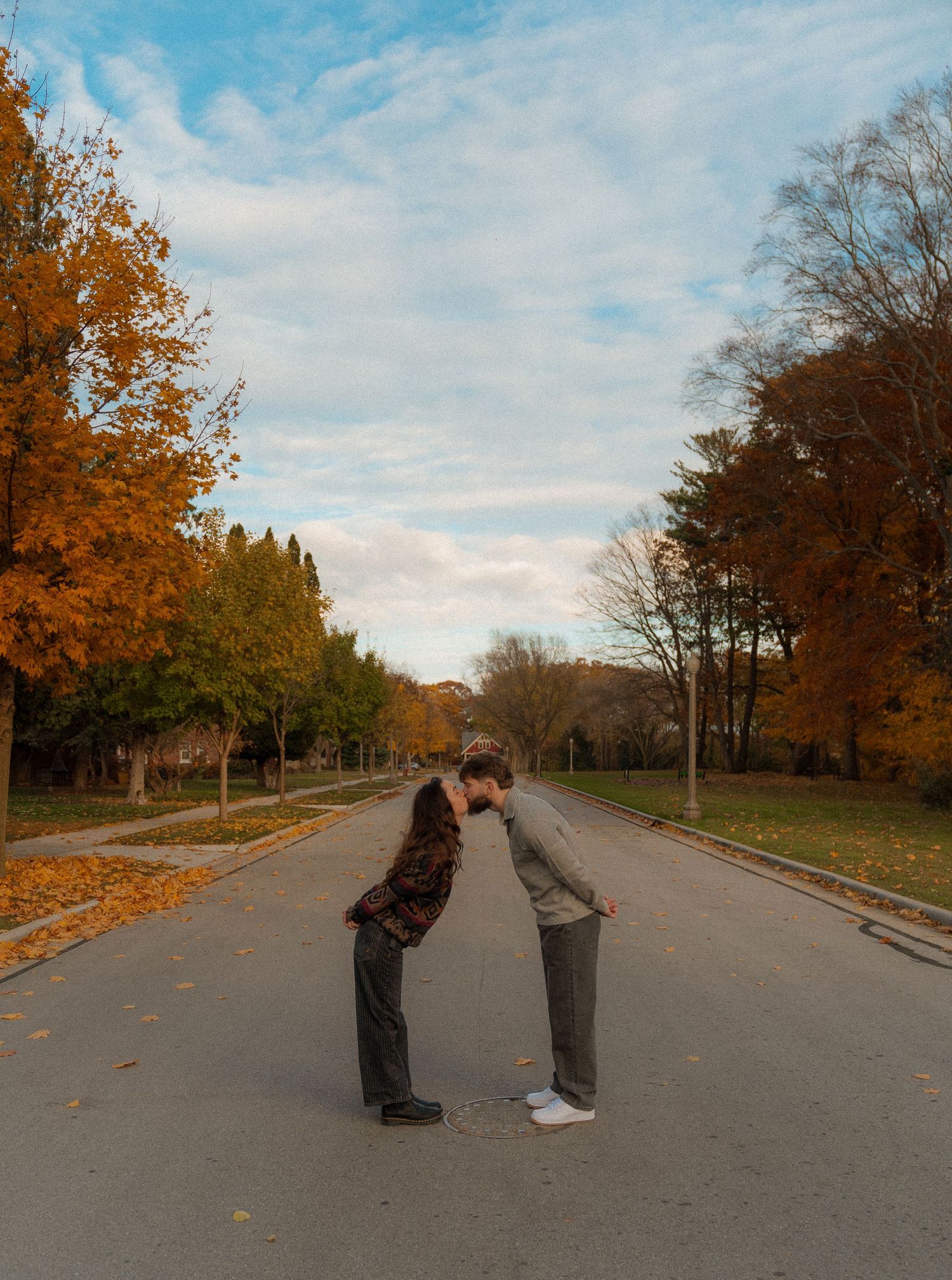 Two people walking on a path surrounded by colorful autumn trees and leaves on the ground.