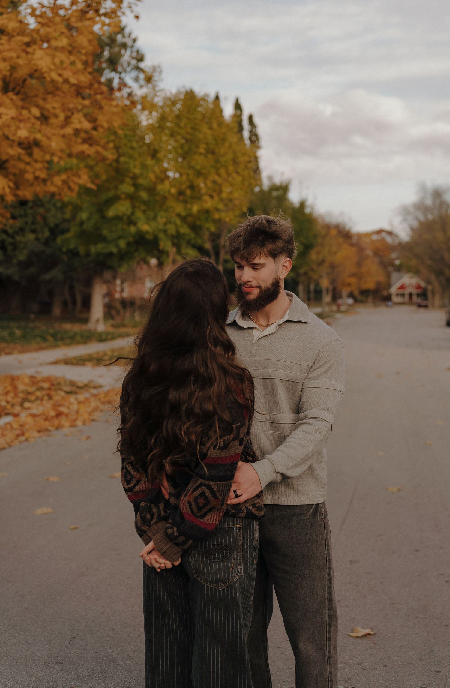 Two people embracing each other in an autumn setting with trees and a road in the background.