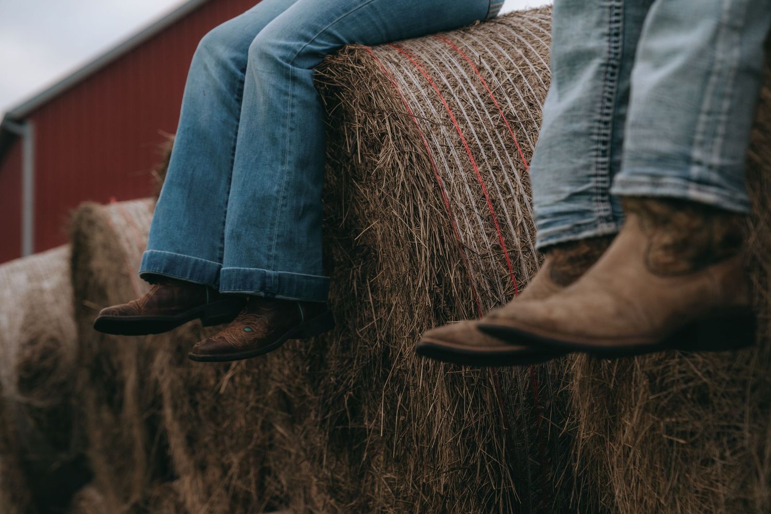 A close-up view of a person's legs wearing cowboy boots and blue jeans, sitting on a wooden structure.
