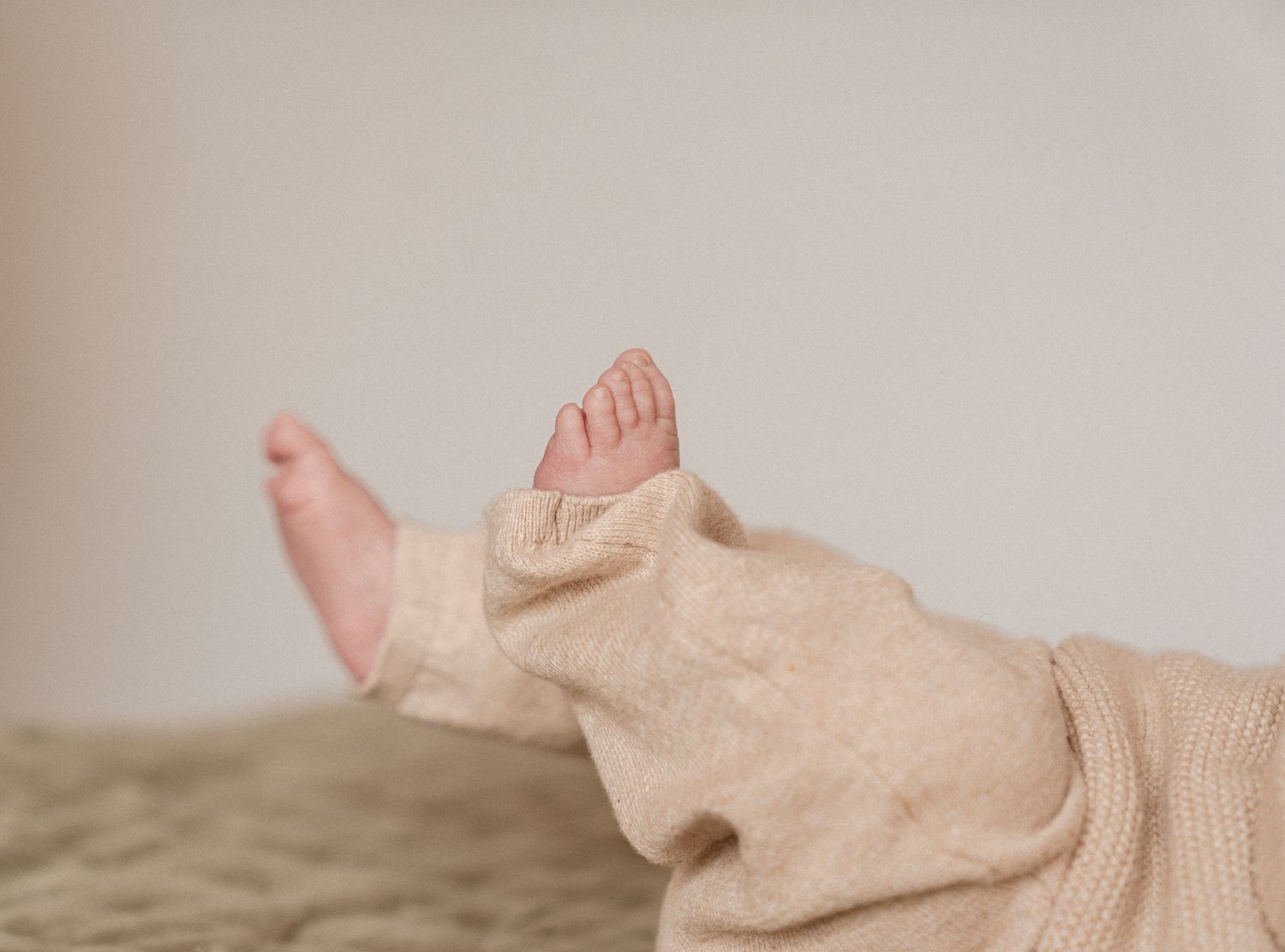 A close-up view of a baby's feet and legs wrapped in a beige blanket or fabric.