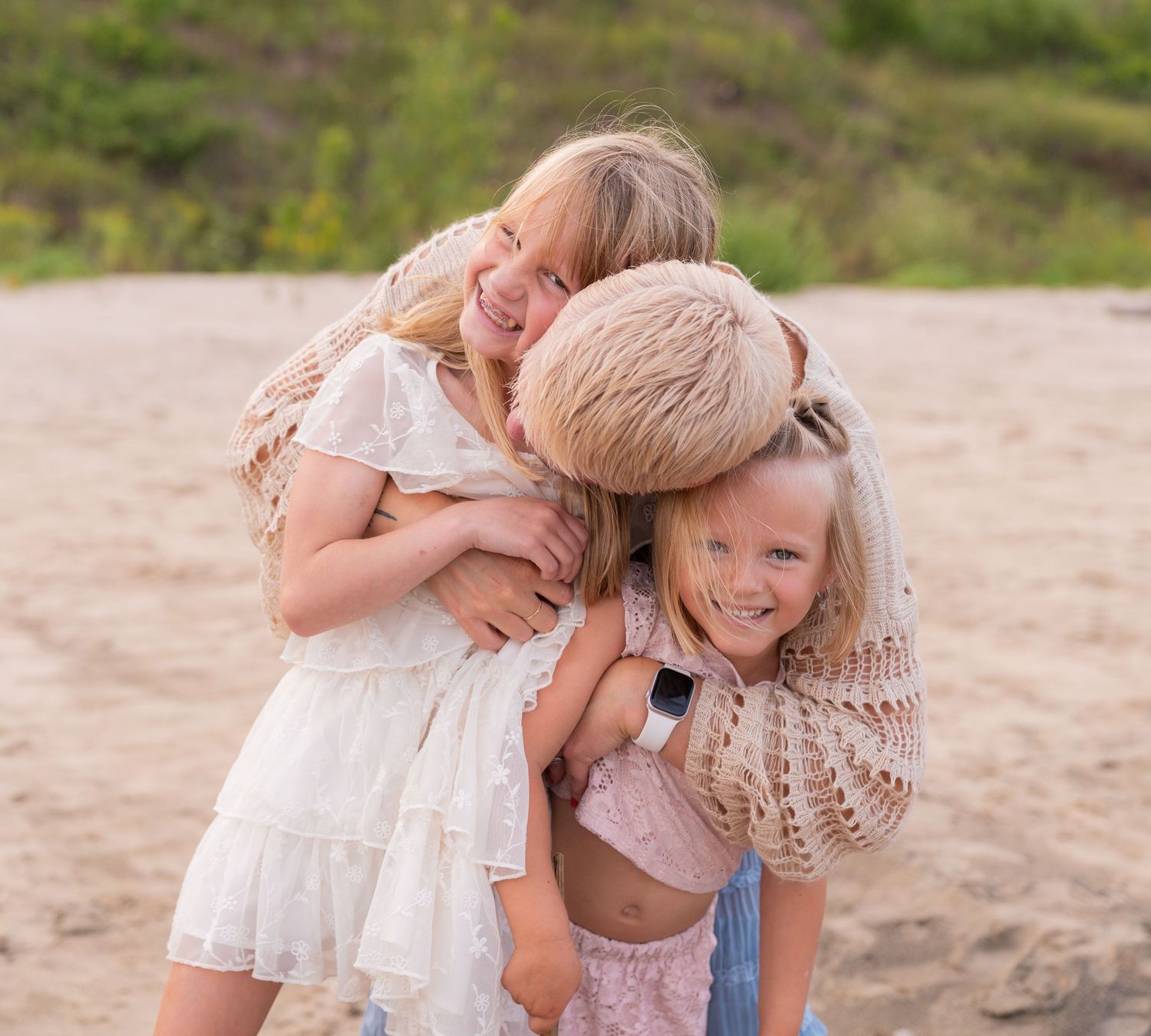 Two young girls wearing white dresses and embracing on a sandy beach.