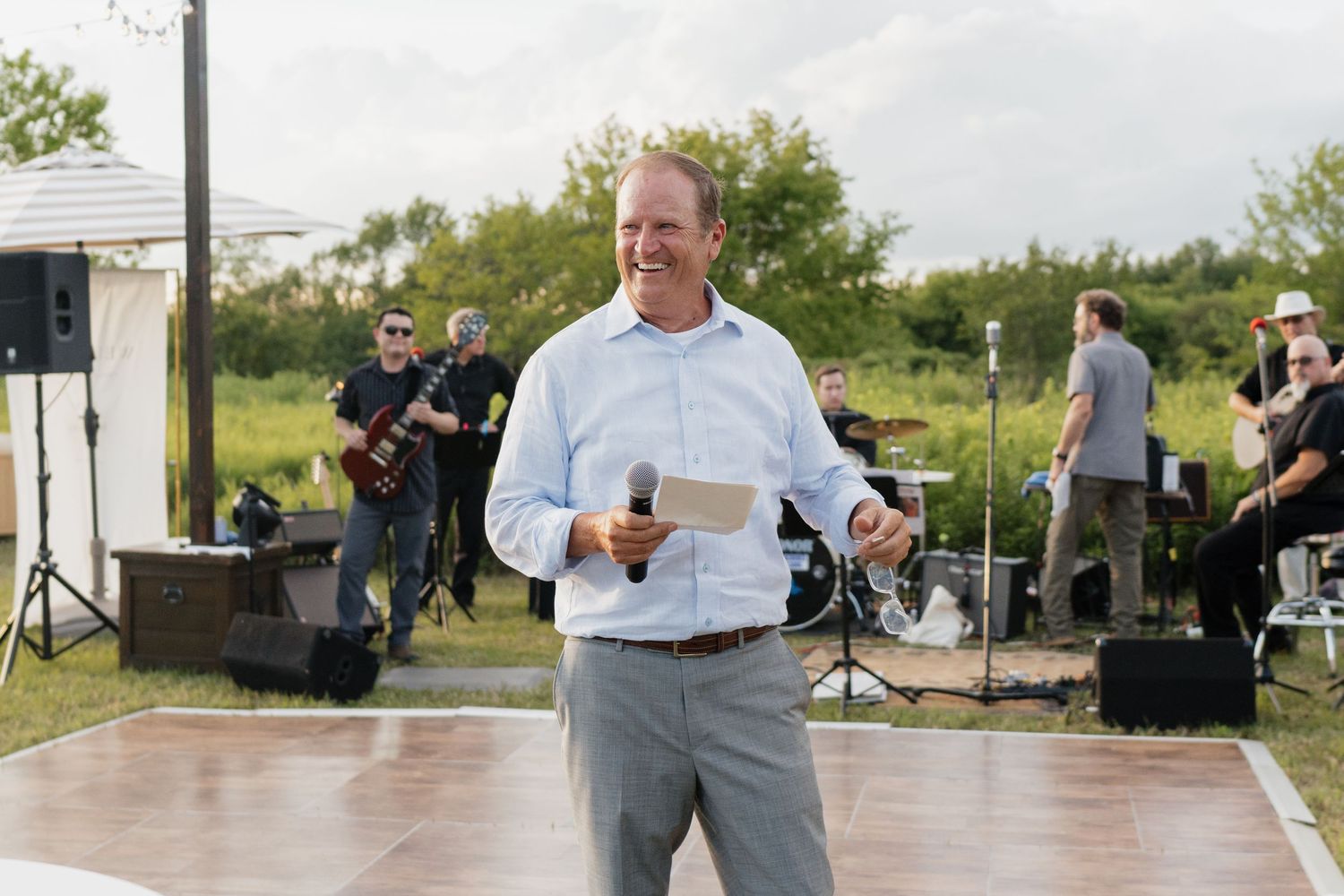 A man in a white shirt and gray pants stands in front of a stage with musical equipment.