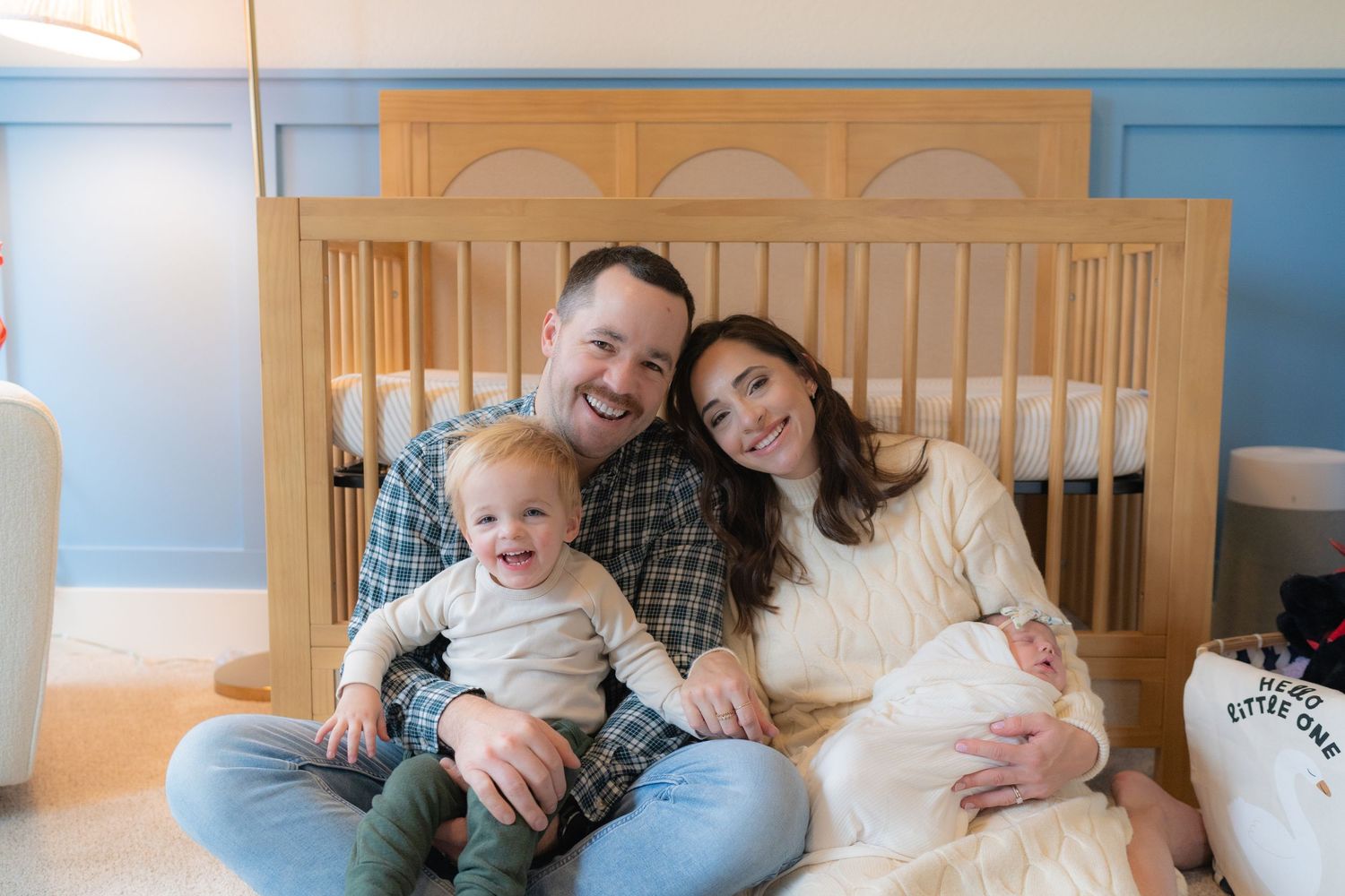 A happy family of three, with a smiling mother, father, and infant child, sitting together in a cozy nursery.