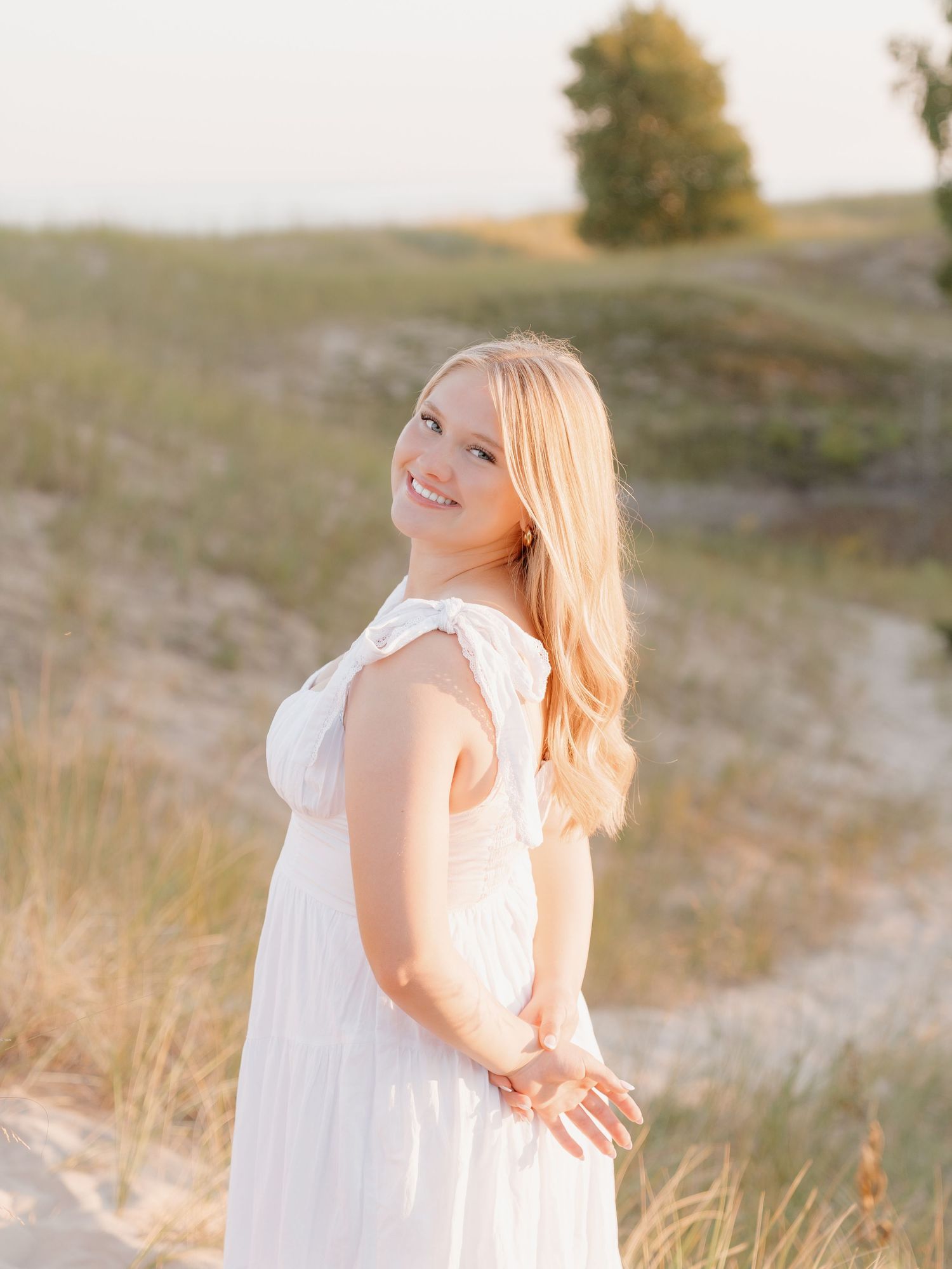 A smiling woman with long blonde hair stands in a field on a sunny day.