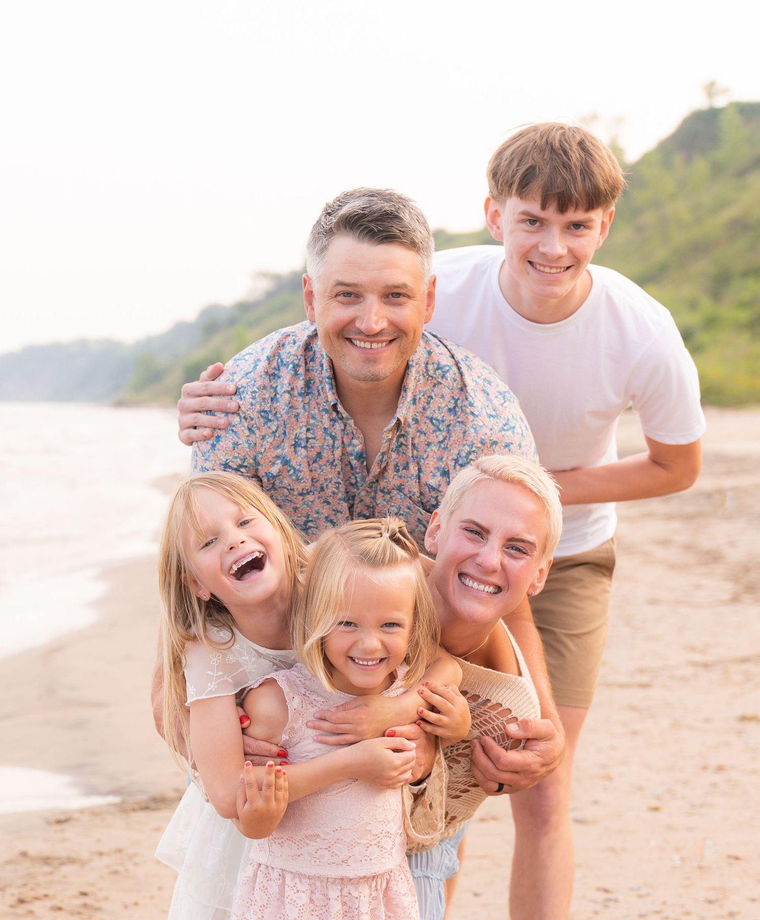 A happy family enjoying a sunny day on the beach, with a mother, father, and three children laughing and smiling together.