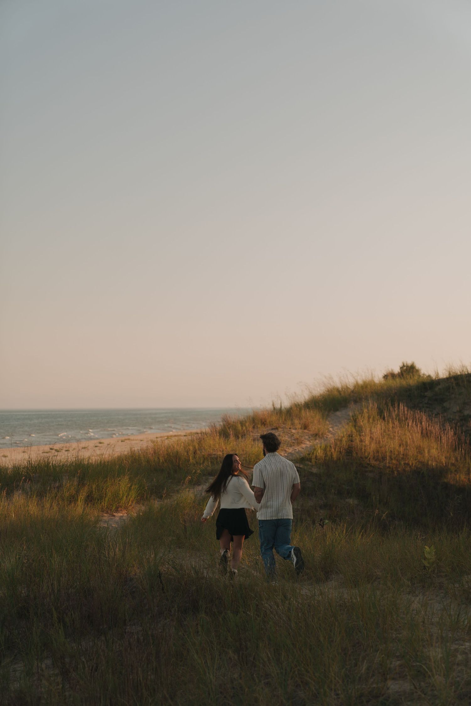 Two people walking on a grassy path along the coastline at sunset.