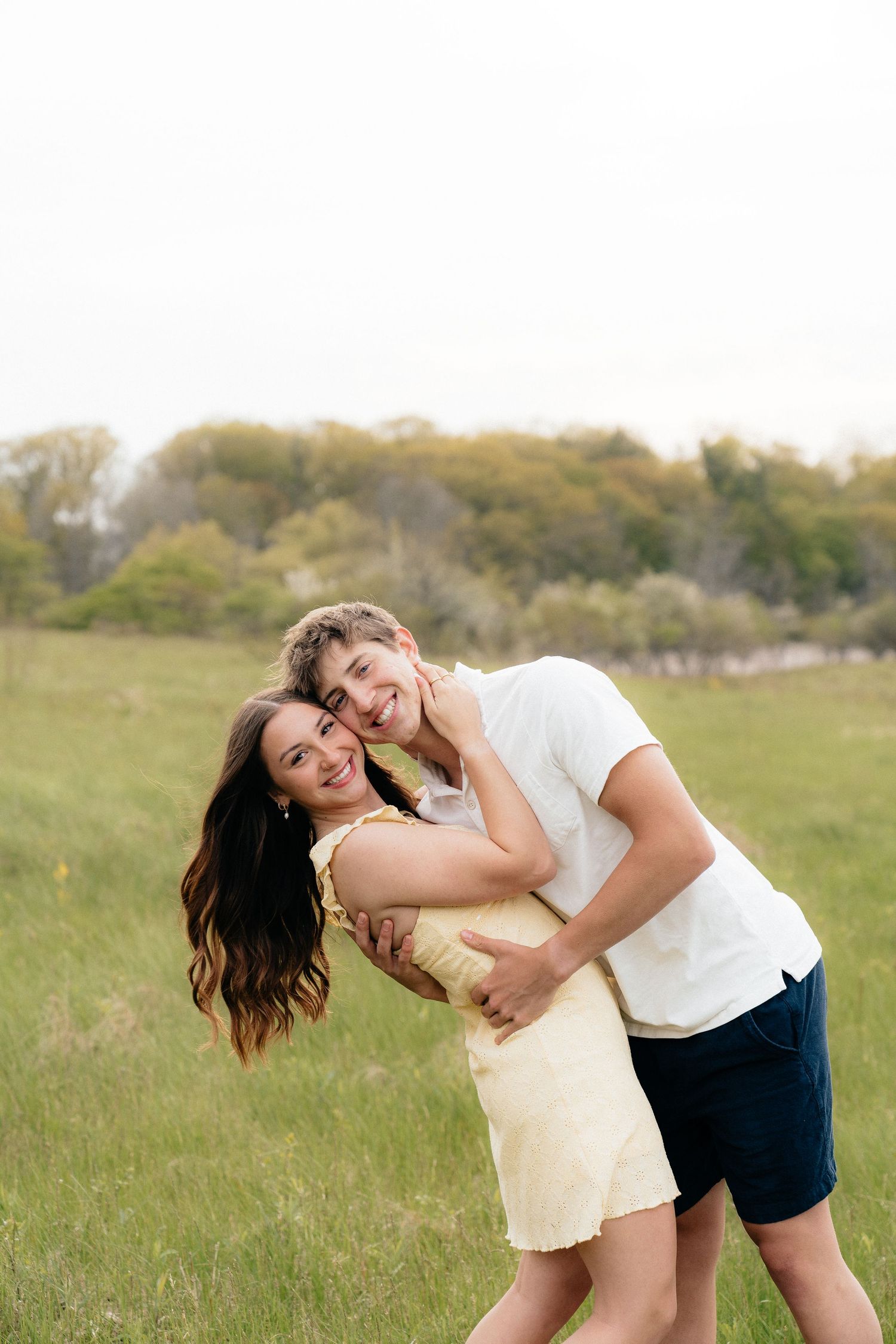 A happy young couple embracing and smiling in a green field, wearing casual summer outfits.