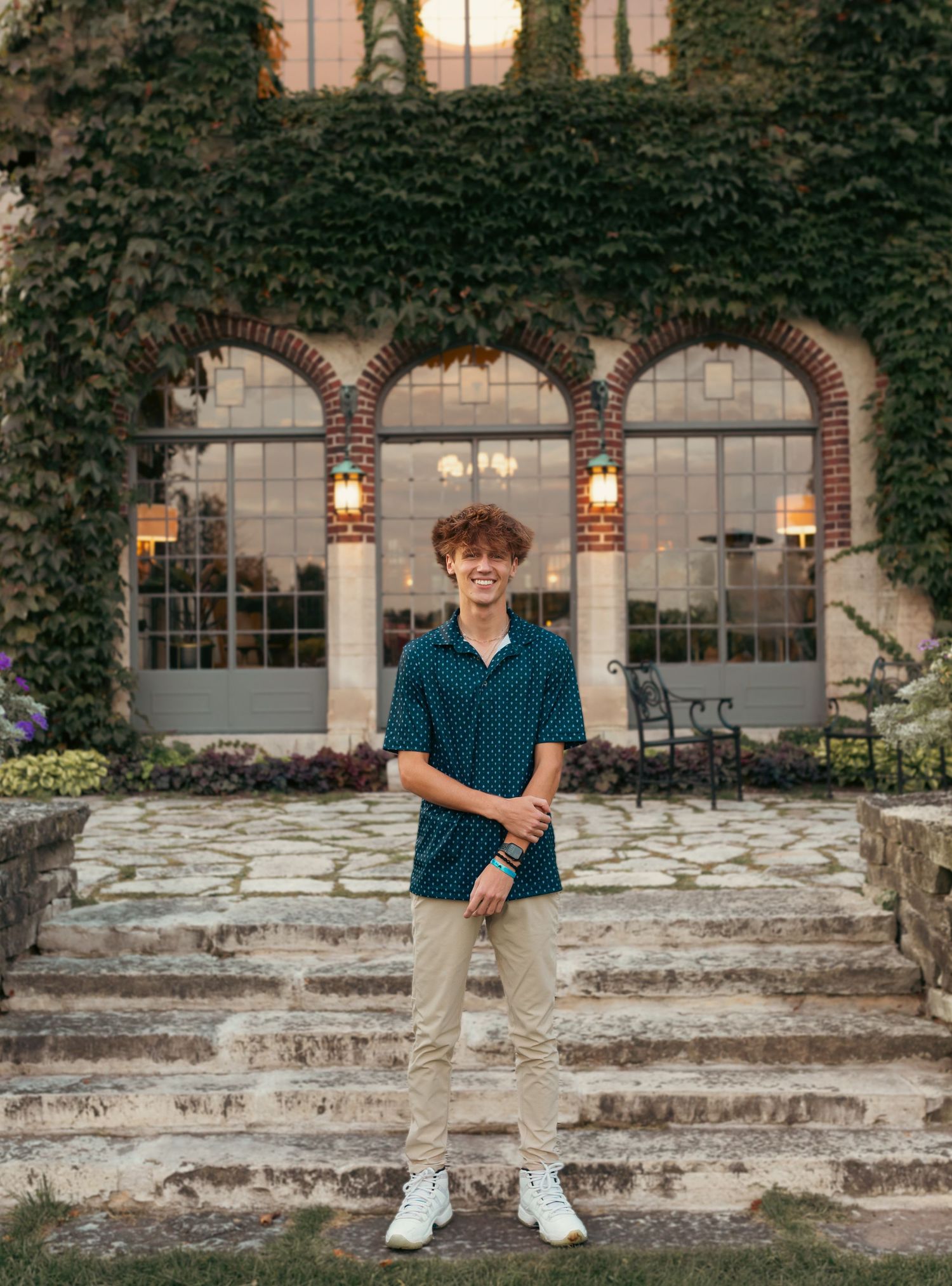 A young man standing on stone steps in front of an ivy-covered building with arched windows.