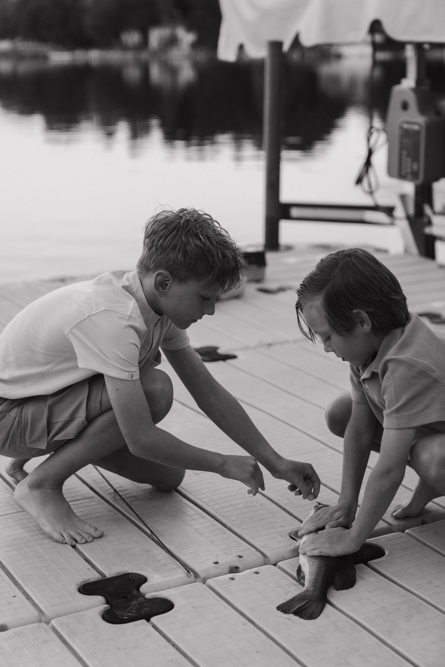 Two young boys playing on a wooden dock by the water in a black and white photograph.