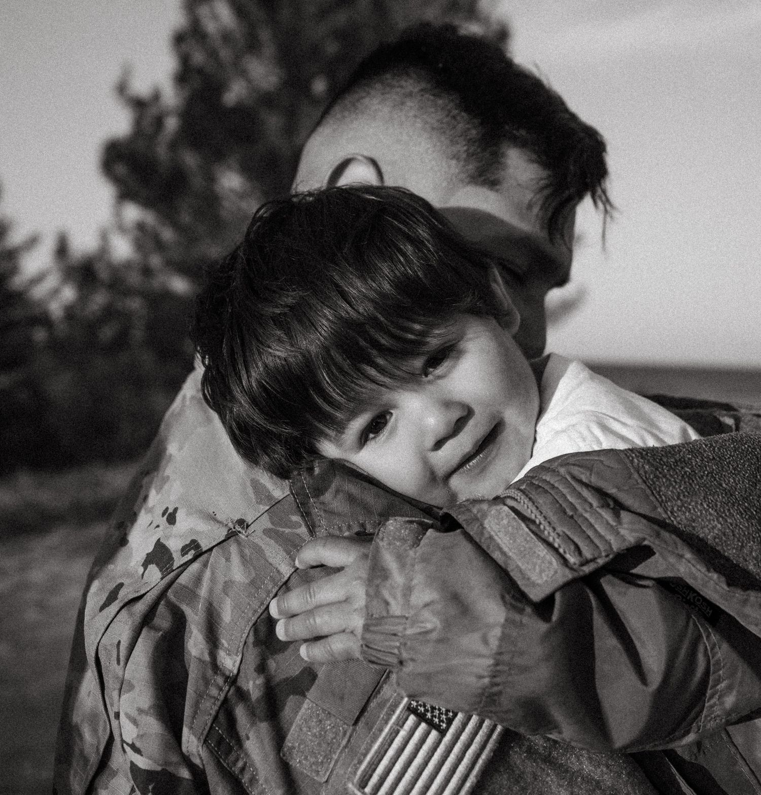 Black and white photo of a child hugging a military soldier in uniform, showing an emotional reunion moment.