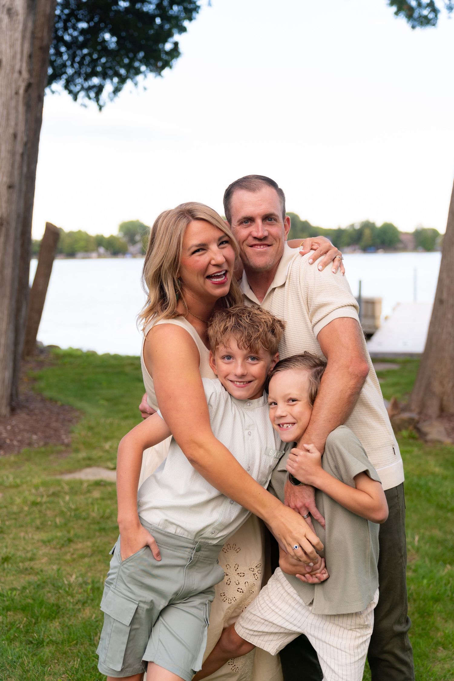 A happy family of four, including a mother, father, and two young children, embracing outdoors in a scenic natural setting.