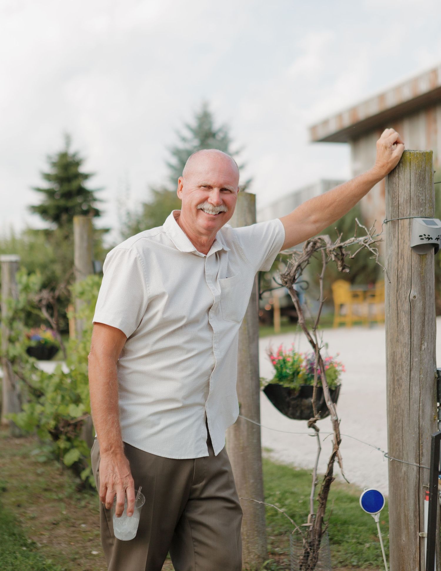 A smiling older man standing in a garden near a wooden fence.