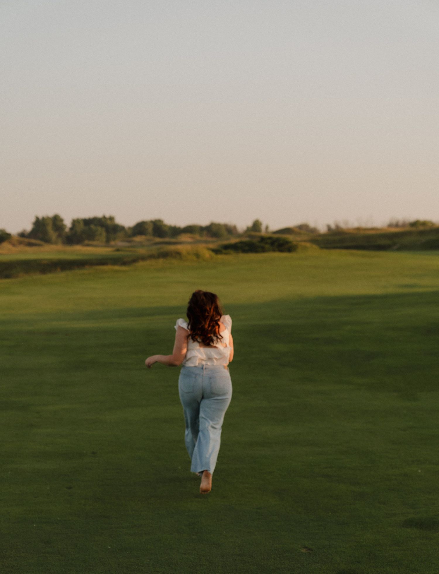 A woman walks across a grassy field on a sunny day.