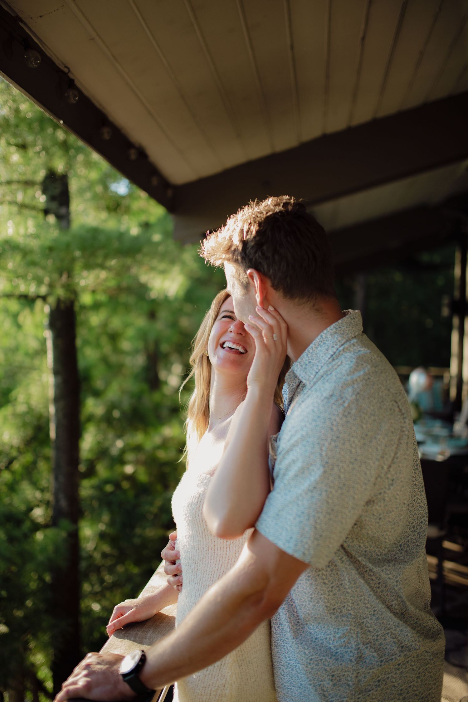 A couple embracing and laughing on a porch surrounded by nature.