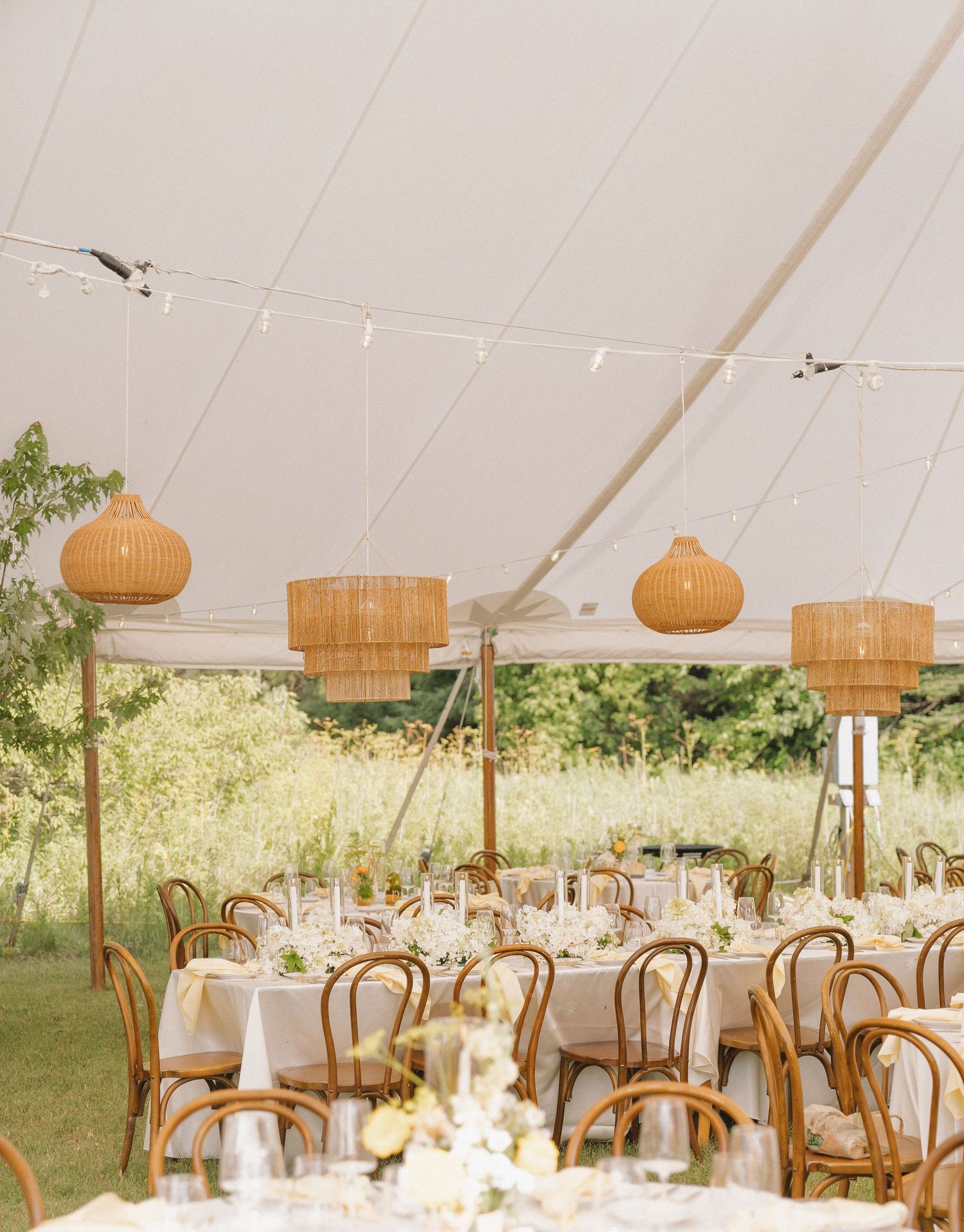 A rustic outdoor wedding reception setup with wooden tables, chairs, and hanging lanterns in a garden setting.