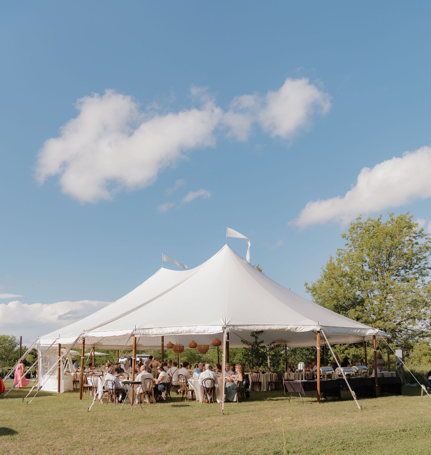 A large white tent set up on a grassy field with trees and a blue sky in the background.