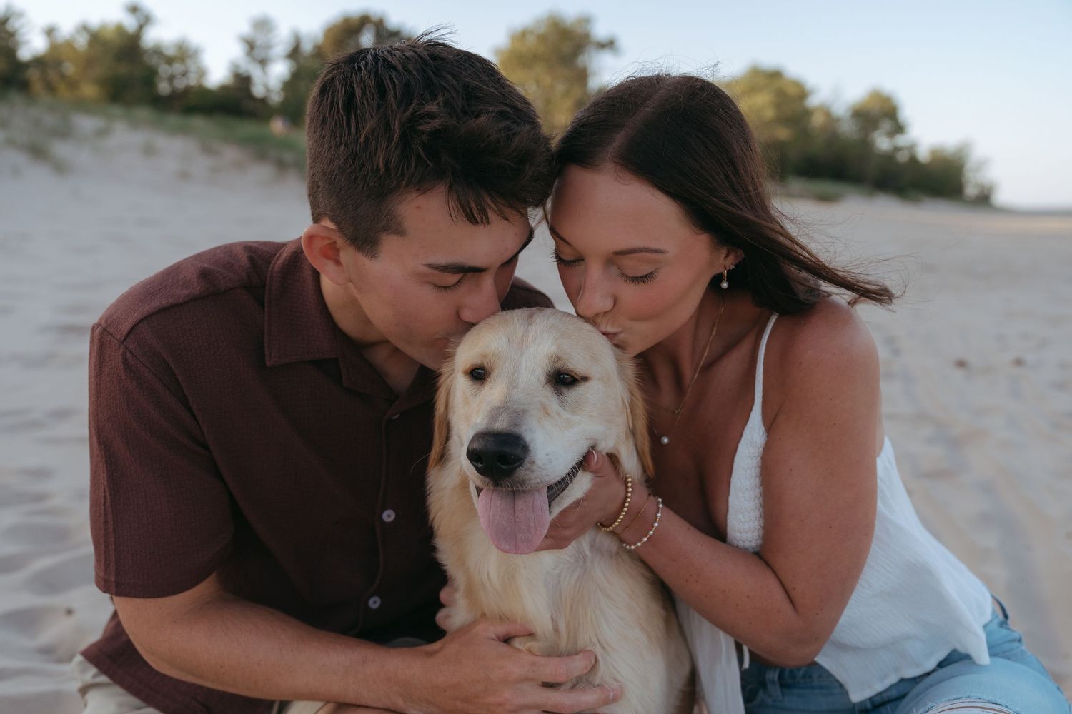 A couple sitting on the beach with their happy dog, enjoying the outdoors together.