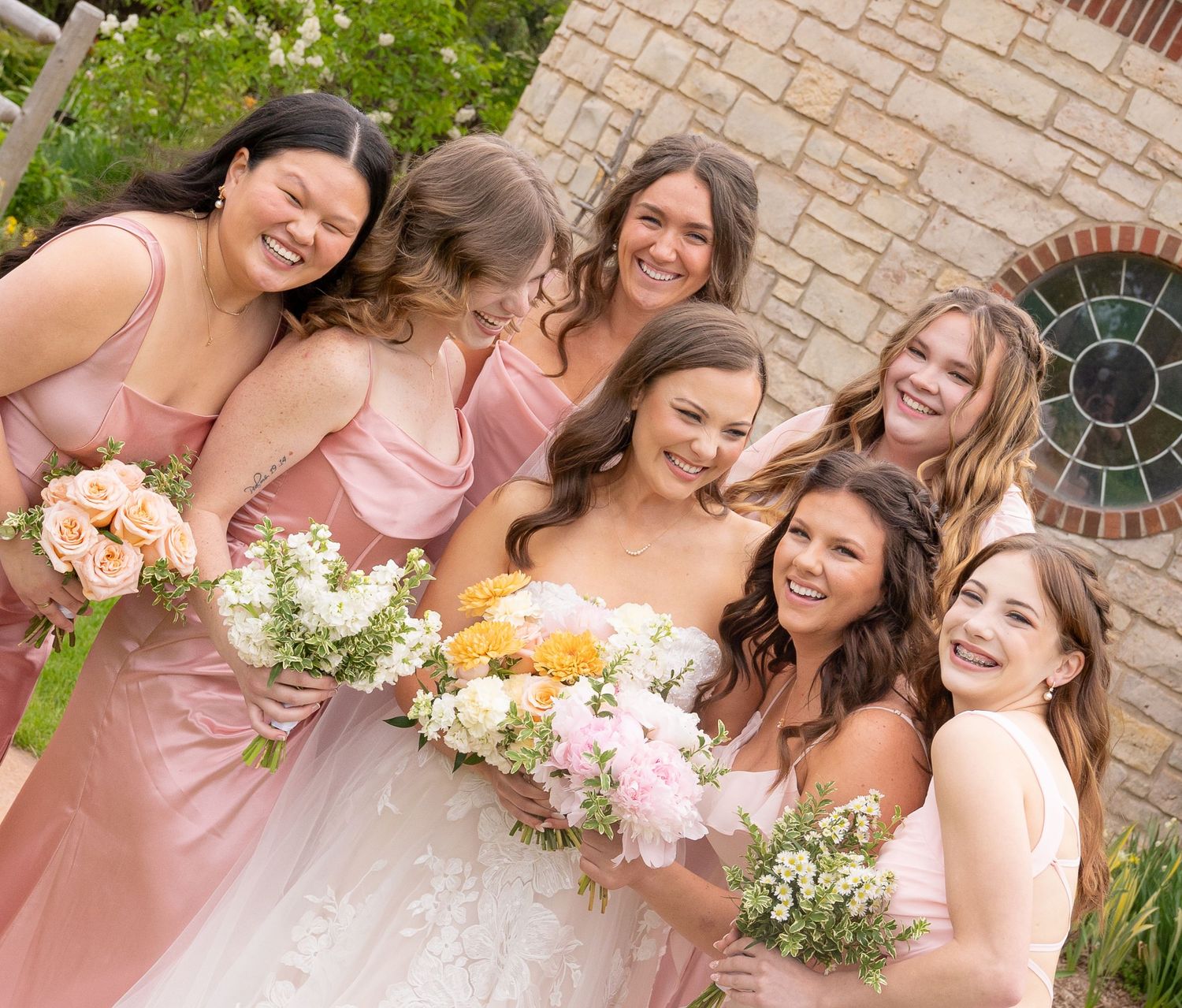 A group of bridesmaids in pink dresses standing together and holding bouquets of flowers.