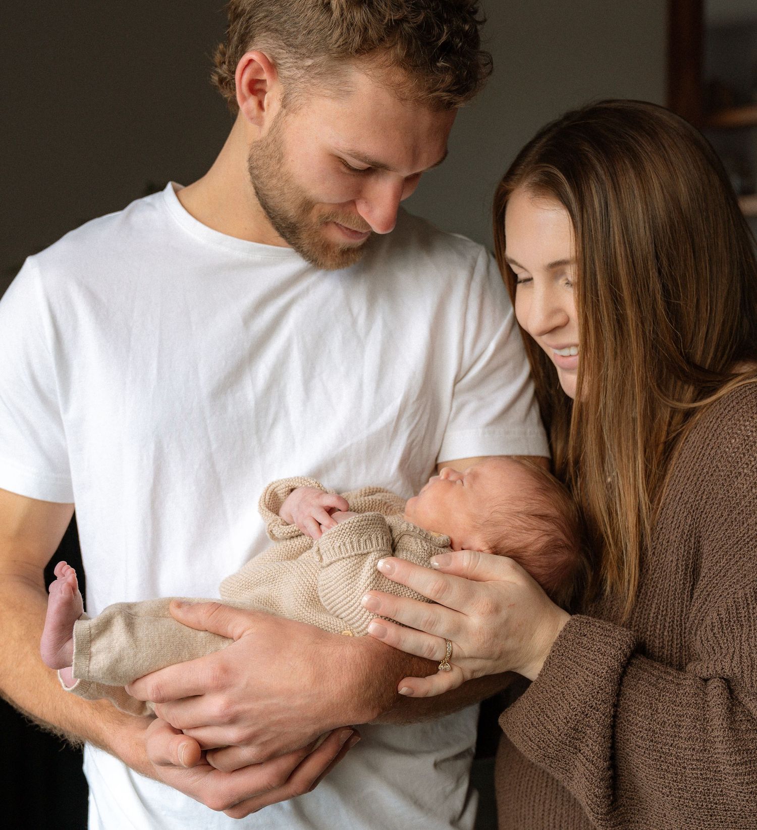 A man and woman are holding a newborn baby in their arms, displaying a tender family moment.