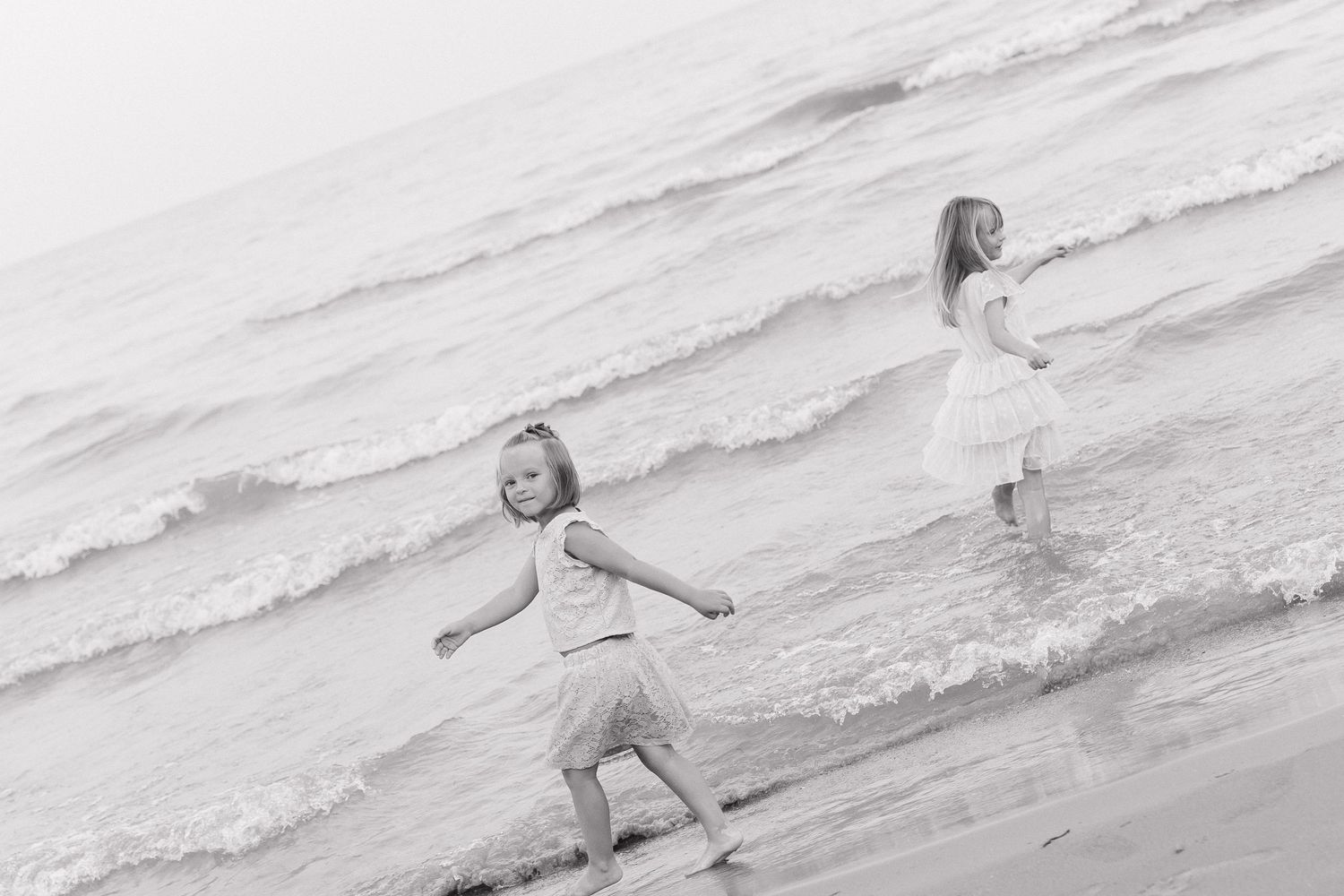 Two children playing on the beach, one running and one standing in the waves.