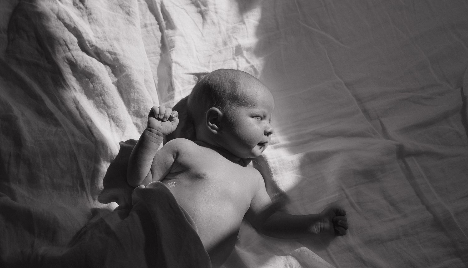 A newborn baby lying on a soft, dark blanket, with a peaceful expression on their face.