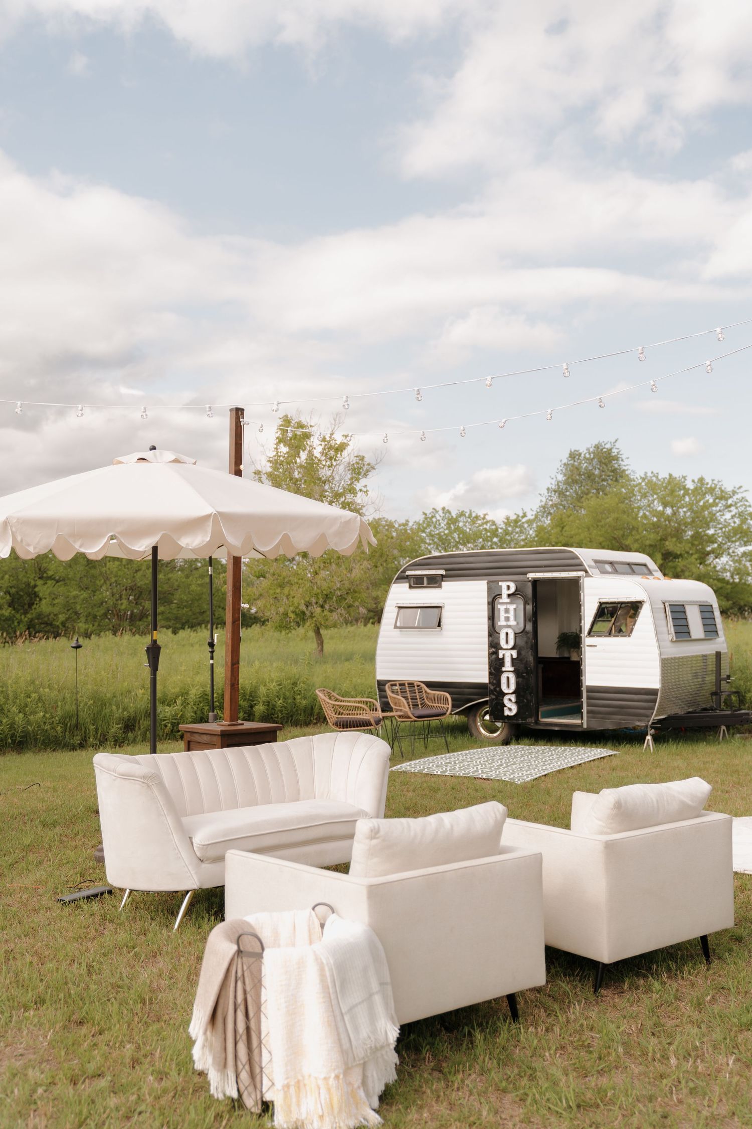 A vintage camper trailer parked in a grassy field with a patio set and umbrella, creating a cozy outdoor living space.