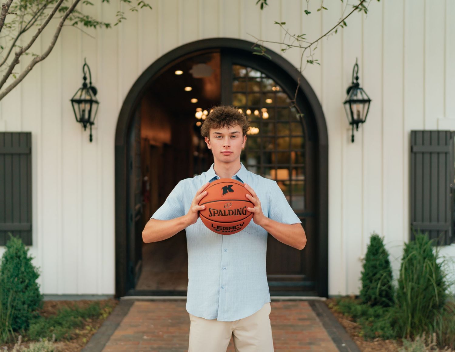 Young man holding a Spalding basketball in front of a white barn-style building with arched door.
