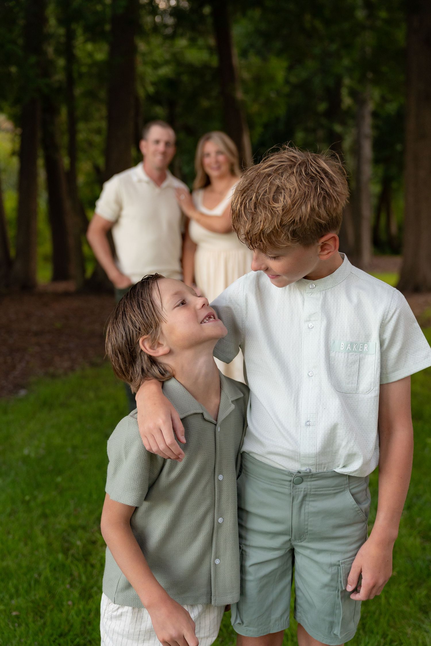 Two young boys embracing in a grassy outdoor setting, with a man and woman in the background.