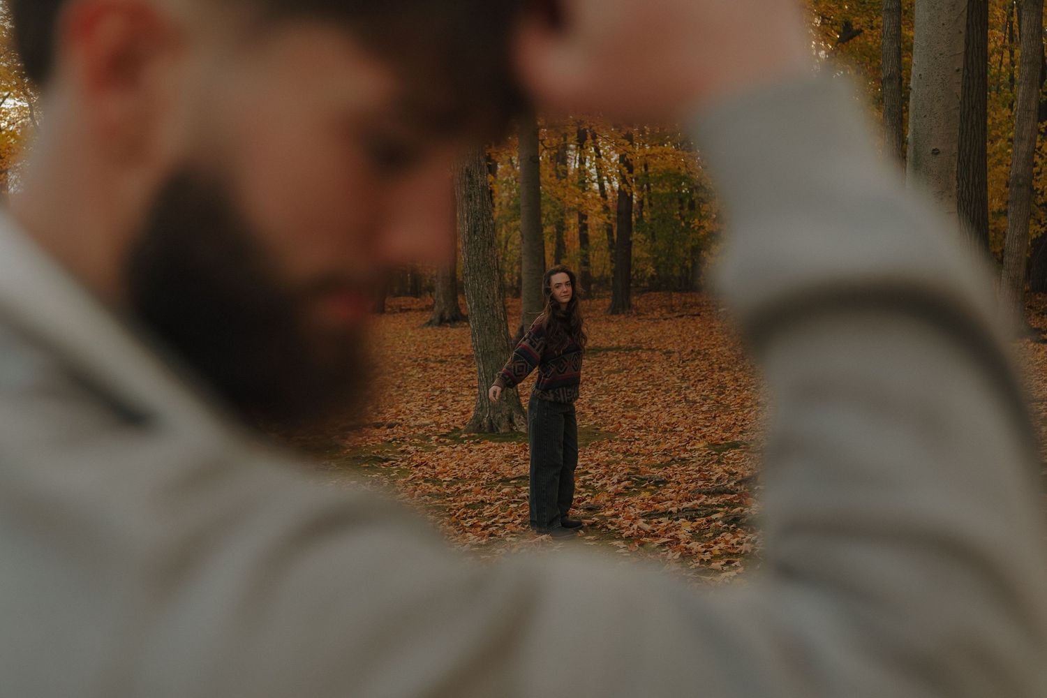 A person walking alone on a path in a forest with fallen leaves on the ground.
