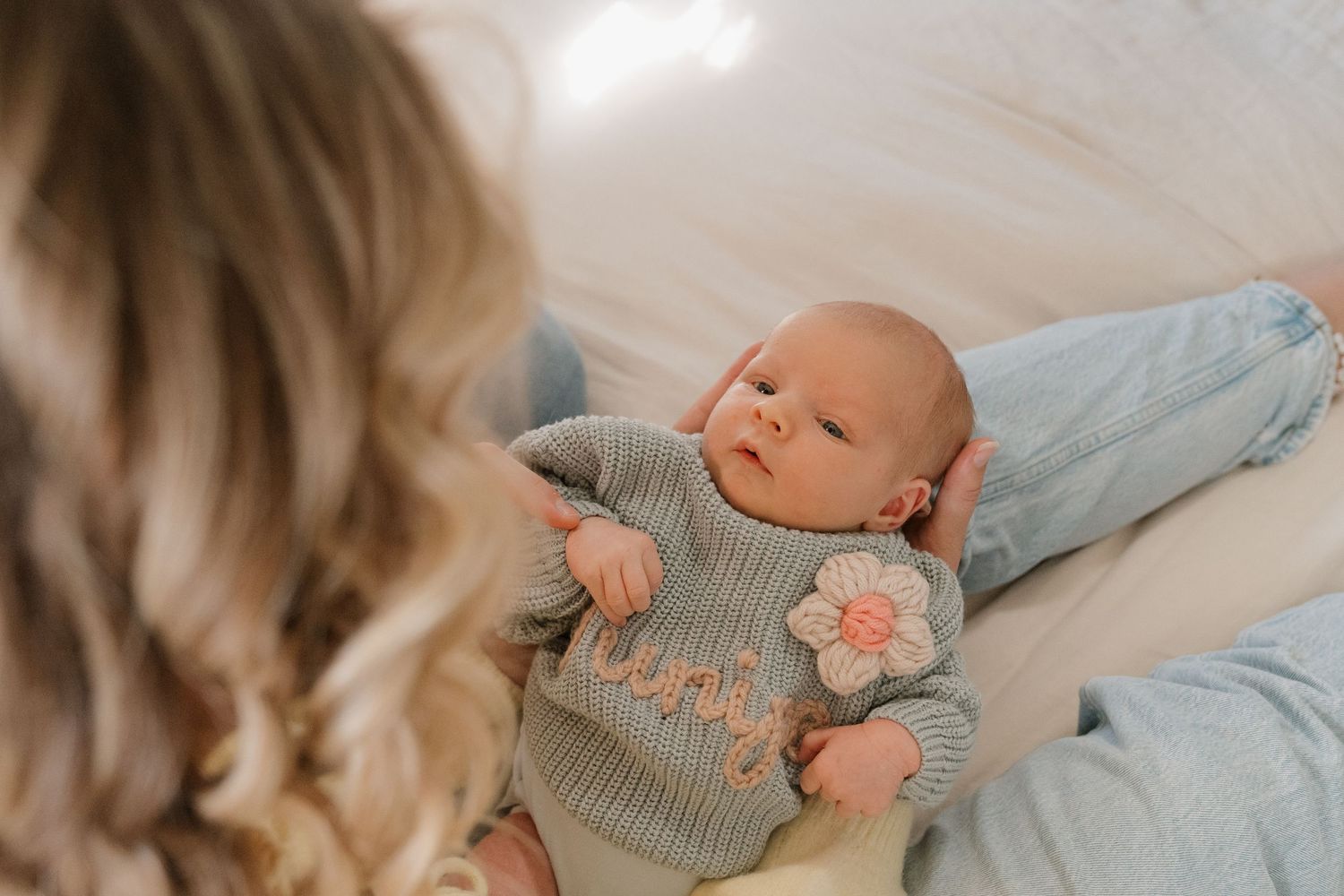 A newborn baby lying on a blanket, being held by a woman's hand.