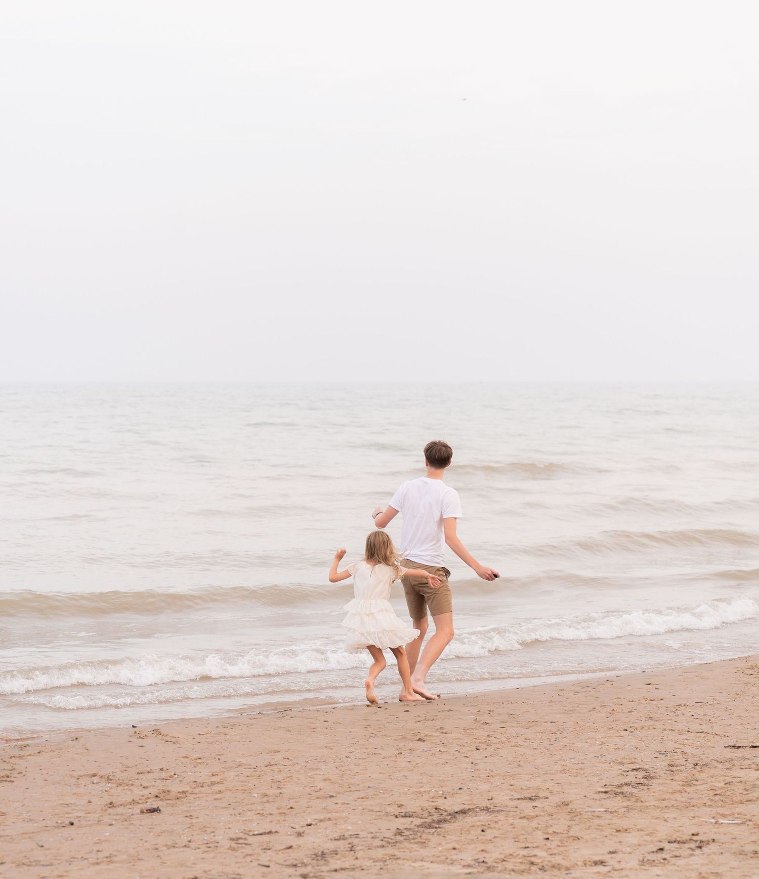 A person and child running along the beach on a misty, overcast day.