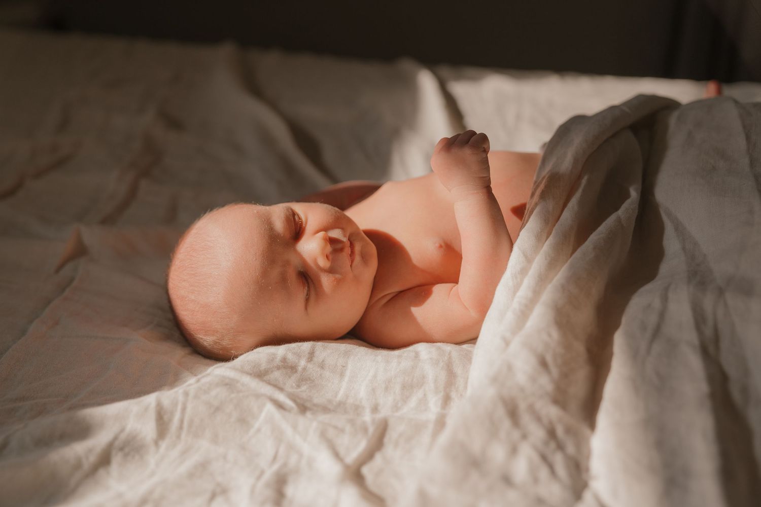 A newborn baby sleeping peacefully on a soft, white blanket.